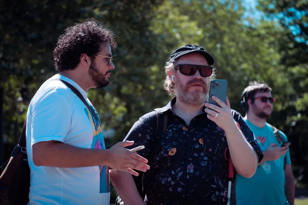 Author Andy Slater testing Space-Time Adventure Tours while holding his phone in front of him, Julian Ochoa standing next to him, talking.